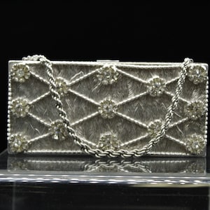 May include: A silver clutch purse with a chain strap and a diamond-like pattern. The purse is decorated with small, clear rhinestones.