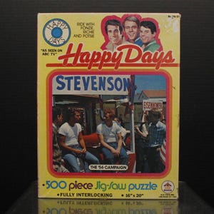 May include: A 500-piece jigsaw puzzle featuring the cast of the television show Happy Days. The puzzle box is yellow with red and blue accents. The image on the box shows the four main characters from the show, Fonzie, Richie, Potsie, and Ralph Malph, standing in front of a red, white, and blue campaign sign that says "Stevenson". The puzzle is fully interlocking and measures 16 inches by 20 inches.