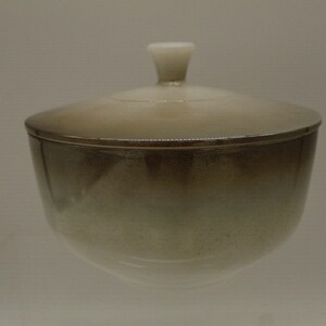 May include: A ceramic bowl with a lid. The bowl is a light brown color with a white glaze. The lid has a small knob on top.