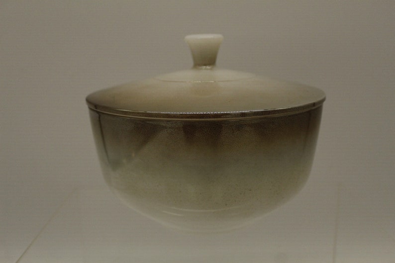 May include: A ceramic bowl with a lid. The bowl is a light brown color with a white glaze. The lid has a small knob on top.