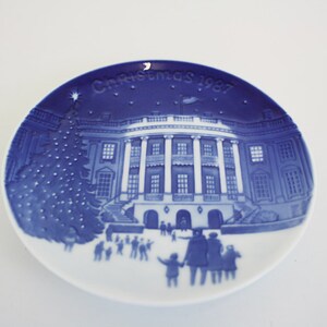 May include: Blue and white porcelain Christmas plate featuring a depiction of the White House with a Christmas tree in front of it. The plate has the text "Christmas 1987" on it.