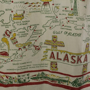 May include: Cream-colored map of Alaska with red, yellow, and green details. Features include cities, landmarks, and text such as "Alaska Range" and "Gulf of Alaska." Includes illustrations of a whale, totem poles, and a treasure chest.