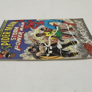 May include: A vintage comic book titled "Spider-Man Storm and Power Man" with colorful illustrations of superheroes in action. The cover features Spider-Man, and other characters in a dynamic battle scene. The comic book is in good condition.