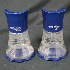 May include: Two blue glass and plastic salt and pepper shakers with a white etched floral design. The shakers have a blue top and a clear glass bottom. The label on the shakers reads "Temptations" by "Tilda".
