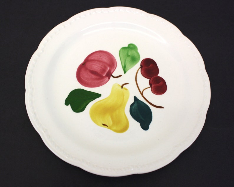 A white Stetson plate from the 1940s. Scalloped edge. Hand-painted with a red apple, yellow pear, two red cherries and three green leaves. A few utensil marks.