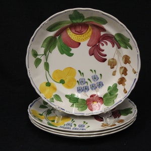 May include: Set of four white ceramic dinner plates with a floral design. The plates feature a variety of flowers in shades of red, yellow, blue, and green.