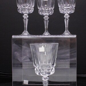 May include: Set of four clear glass wine glasses with a cut crystal design. The glasses are arranged on a clear acrylic platform.