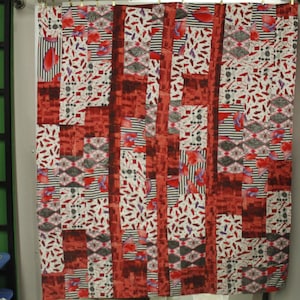 May include: A red, white, and black patchwork quilt with geometric patterns. The quilt is made of different fabrics and has a modern design.