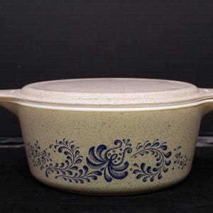 May include: A beige casserole dish with a white lid and a blue floral design. The dish has a speckled finish.