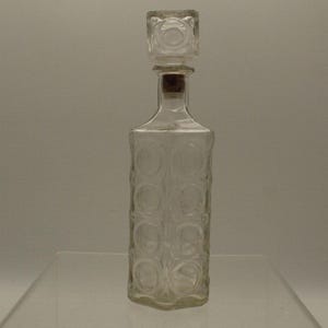 May include: A clear glass decanter with a square stopper. The decanter has a textured design with circular patterns.
