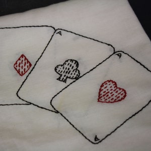 May include: Three embroidered playing cards, each with a different suit: a diamond, a club, and a heart. Each card is an ace and has a black outline.