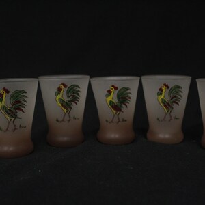 May include: Set of five frosted glass shot glasses with a rooster design. Each glass features a yellow rooster with green and red accents on a brown background.