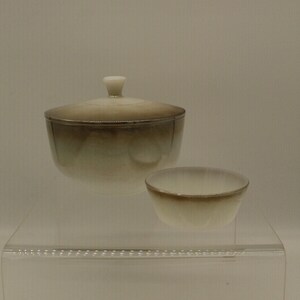 May include: A set of two ceramic bowls with a gradient glaze. The larger bowl has a lid and the smaller bowl is open. The bowls are a light brown color with a white rim.