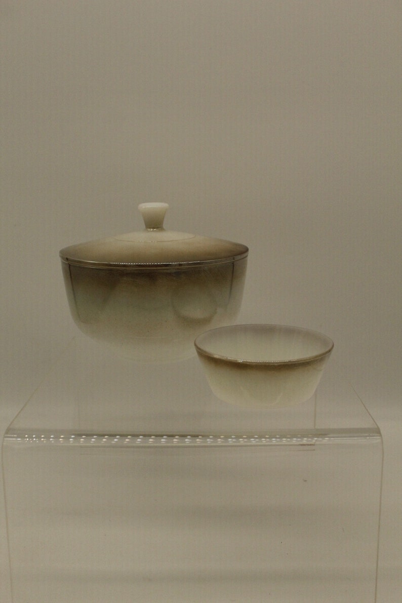 May include: A set of two ceramic bowls with a gradient glaze. The larger bowl has a lid and the smaller bowl is open. The bowls are a light brown color with a white rim.