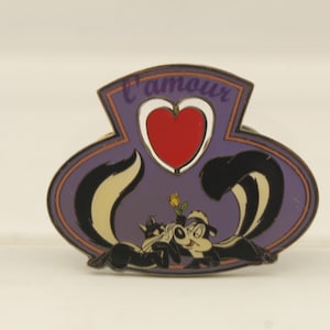 May include: A purple and gold enamel pin featuring Pepe Le Pew and Penelope Pussycat with a red heart and the text "L'amour" above them.
