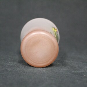 May include: The base of a frosted glass vase with a pink tint. The vase features a floral design with yellow, green, and red accents.
