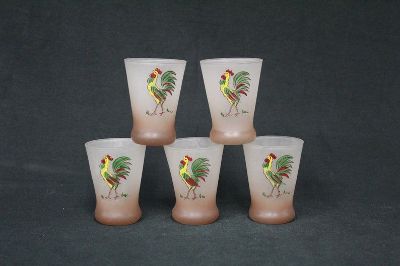 May include: Set of five frosted glass drinking glasses with a rooster design. Each glass features a yellow rooster with red and green accents on a brown background.