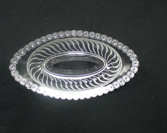 May include: A clear glass oval dish with a beaded edge and a swirl design in the center.