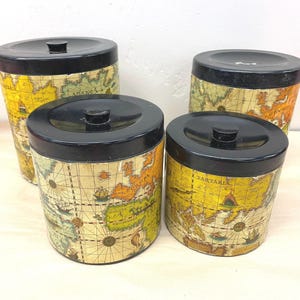 May include: Set of four vintage canisters with black lids. The canisters are cylindrical and feature a world map design in shades of yellow, brown, and green. The map includes illustrations of ships and navigational lines.