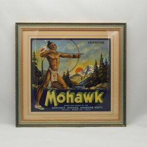 May include: A vintage framed poster advertising Mohawk Valencias oranges. The poster features a Native American man with a bow and arrow in a forest setting with mountains in the background. The text on the poster reads "Mohawk Valencias Grown and Packed by the Santiago Orange Growers Ass'n. Orange, Orange Co., Calif."