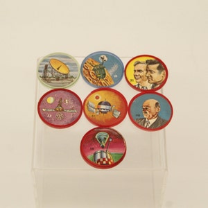 May include: A set of ten round, colorful, paper tokens with images of space exploration, astronauts, and spacecrafts. The tokens have red borders and white numbers on them.
