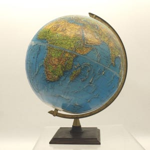 May include: A vintage globe with a detailed map of the world, featuring continents in shades of green, yellow, and brown, set against blue oceans. The globe is mounted on a dark wooden base with a brass-colored metal frame.