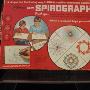 May include: A red box with the words "Kenner's NEW SPIROGRAPH" on the front. The box shows two children drawing with the Spirograph, and examples of the designs that can be created. The text on the box says "A simple and fascinating way to DRAW a million marvelous patterns".
