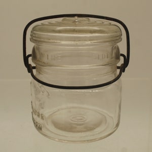 May include: A clear glass jar with a wire bail handle and a glass lid. The jar has the words "WIRE" and "LID" printed on the side.