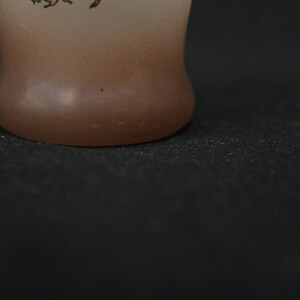 May include: A frosted glass vase with a brown gradient and a floral design. The vase has a rounded bottom and is sitting on a black surface.