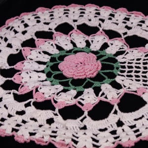 May include: White crochet doily with a pink flower design in the center.