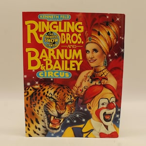 May include: A vintage circus poster featuring a red, white, and yellow color scheme. The poster advertises Ringling Bros. and Barnum & Bailey Circus. The poster features a woman in a red and gold costume, a clown, and a leopard.