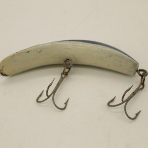 May include: A white and blue fishing lure with two treble hooks. The lure is shaped like a fish and has a textured surface.