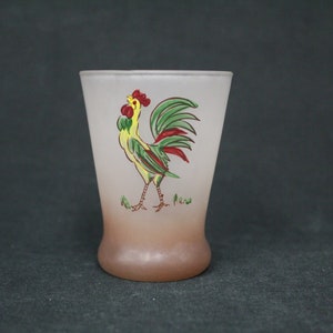 May include: A frosted glass shot glass featuring a rooster design. The rooster is yellow, green and red. The glass has a brown ombre effect at the bottom.