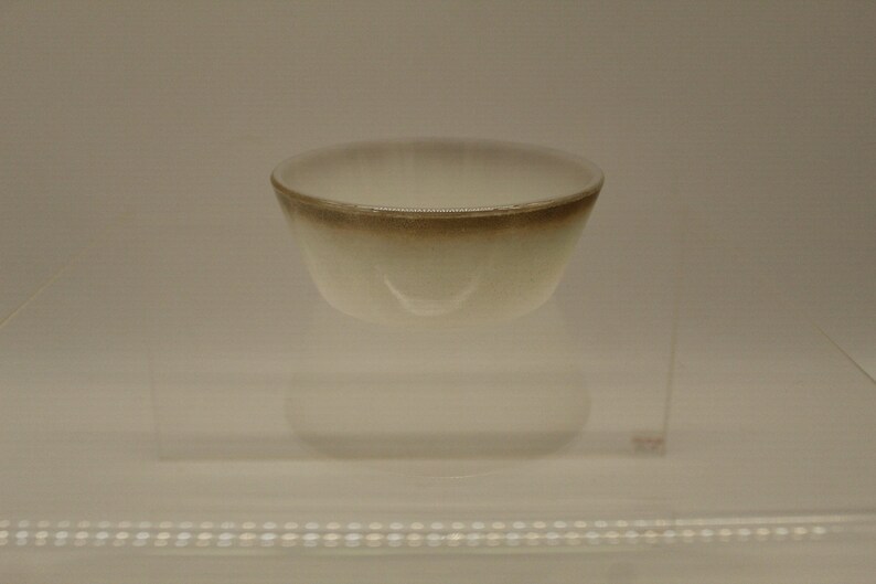 May include: A white ceramic bowl with a brown rim. The bowl is sitting on a clear glass surface.