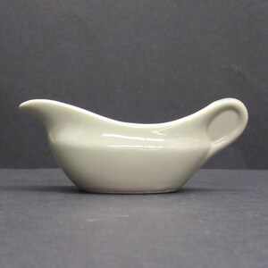 May include: A light gray ceramic gravy boat with a rounded shape and a handle on one side.