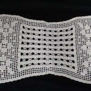 May include: White crocheted doily with a delicate floral pattern. The doily has a square center with a border of intricate lacework.