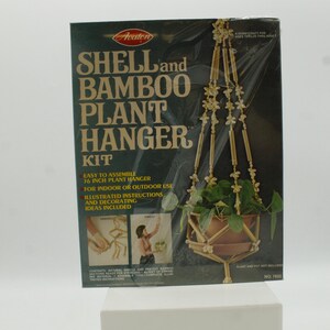 May include: A rectangular box for an Avalon Shell and Bamboo Plant Hanger Kit. The dark green packaging features text, images of the assembled 36 inch hanger, and lists contents including natural shells, bamboo sections, and 45 feet of string.