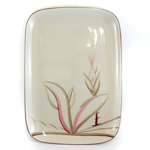 May include: Cream-colored rectangular serving platter with a brown rim and a floral design. The design features pink, brown, and tan stylized flowers and leaves. A decorative piece for serving food.