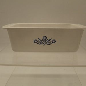 May include: White ceramic loaf pan with a blue floral design. The design features three stylized flowers with blue leaves.