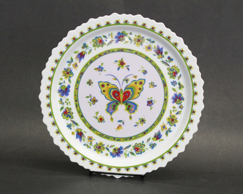 May include: White ceramic serving platter with a scalloped edge. The centre features a colourful butterfly design surrounded by floral patterns in blue, yellow, and red. A green border encircles the butterfly and flowers.
