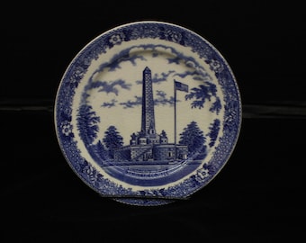 May include: A blue and white oval ceramic plate with a decorative border. The center of the plate features a black and white illustration of the Lincoln Tomb in Springfield, Illinois.