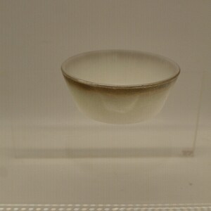 May include: A small, white ceramic bowl with a brown rim. The bowl is sitting on a clear glass platform.