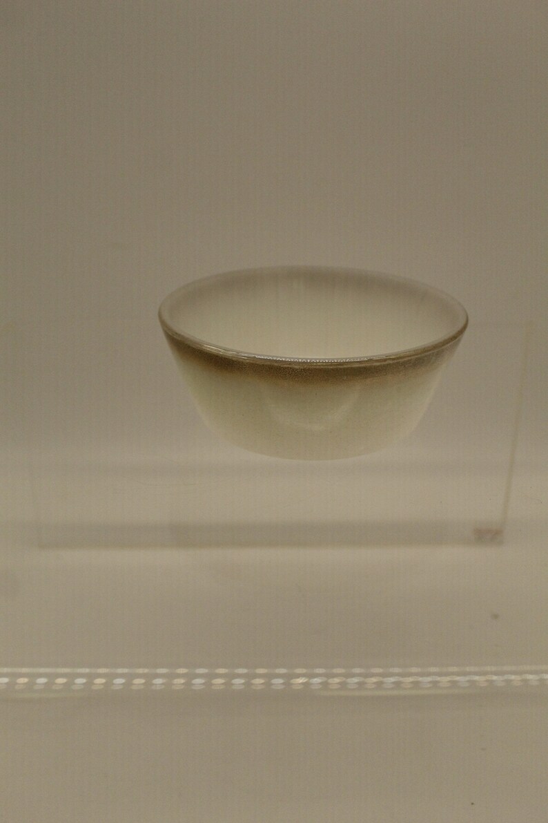 May include: A small, white ceramic bowl with a brown rim. The bowl is sitting on a clear glass platform.