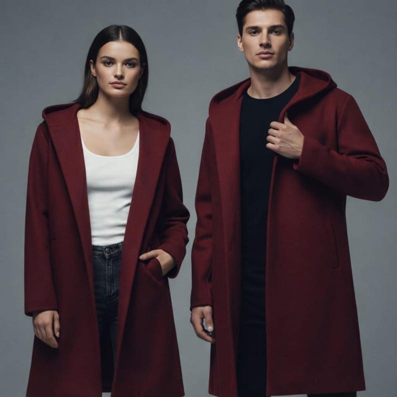 Puede incluir: Dos personas vestidas con abrigos largos con capucha de color burdeos. Los abrigos tienen un dise&ntilde;o sencillo y elegante con un corte entallado. La mujer lleva una camiseta sin mangas blanca y vaqueros oscuros. El hombre lleva una camiseta negra.