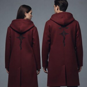 Puede incluir: Abrigo con capucha burdeos con un dise&ntilde;o bordado en negro en la espalda. El abrigo tiene una silueta larga y entallada y una capucha. El dise&ntilde;o es una cruz estilizada con una serpiente. El abrigo lo llevan dos personas, de espaldas a la c&aacute;mara.