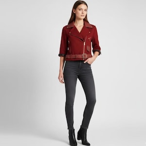 May include: A burgundy-colored jacket with a brown leather collar and belt. The jacket has a zipper closure and three-quarter sleeves. The model is wearing dark gray skinny jeans and black ankle boots.