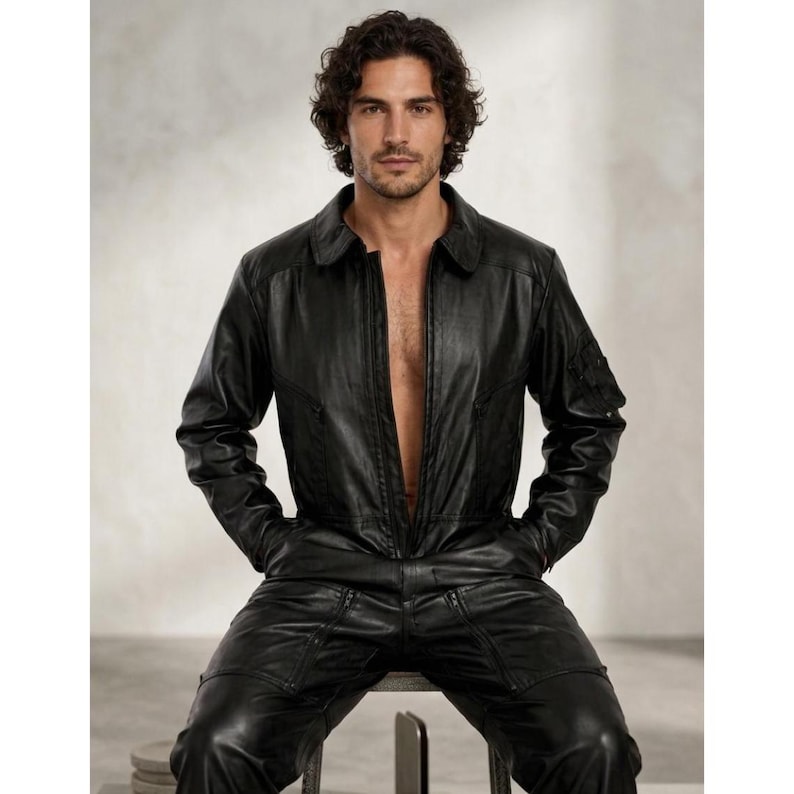 May include: Black leather jumpsuit with a collared neckline and a front zipper. The one-piece garment features multiple pockets and a tailored fit. The model is wearing the jumpsuit while seated on a stool.