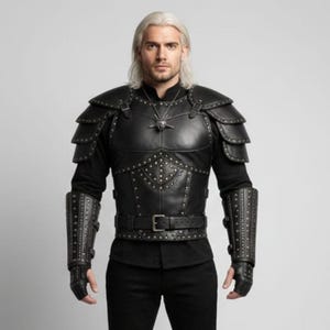 May include: Black leather armour set with studded details, including a chest piece, shoulder pads, arm guards, and belt. The armour is worn over a black shirt and trousers. A silver pendant hangs from the neck.