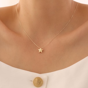 May include: A delicate gold necklace with a small, five-pointed star pendant. The star is suspended from a fine gold chain, creating a minimalist design. The necklace is displayed against a neutral background.