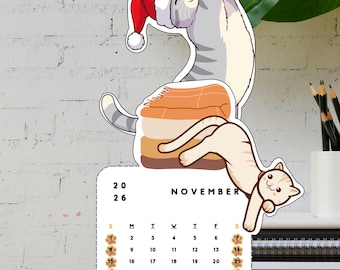 May include: A November calendar featuring cartoon cats. One cat wears a Santa hat, another is on top of a sushi roll. The calendar has a white background with the days of the week and the word "November". The calendar is on a wooden surface.